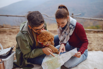 Young cute multicultural couple in love sitting on blanket and looking at map. Picnic at autumn...