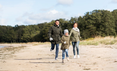 family, leisure and people concept - happy mother, father and little daughter running along autumn beach