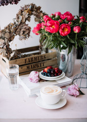 Delicious strong morning espresso coffee, fresh summer cherries and strawberries, coral peonies bouquet, pile of magazines and a glass of water on the pink table background