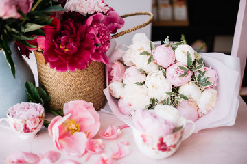 Beautiful pink peonies in a blue vase, magenta peonies in a wicker basket, peony in a cup and beautiful big white and pink peonies bouquet on the pink table  with petals around it