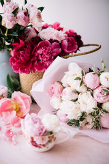 Beautiful pink peonies in a blue vase, magenta peonies in a wicker basket, peony in a cup and beautiful big white and pink peonies bouquet on the pink table  with petals around it