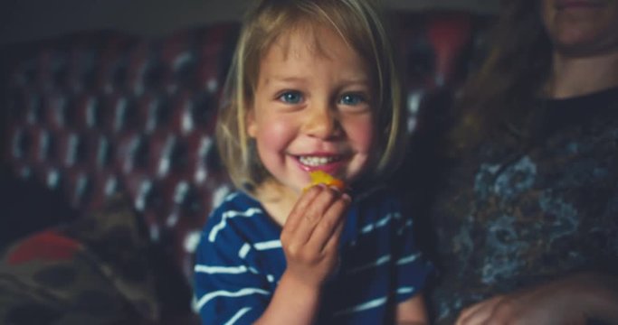Little toddler eating fruit with his mother on sofa at home