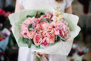 Very nice young woman holding beautiful tender blossoming bouquet of fresh hydrangeas, roses, carnations, peonies, eucalyptus, eustoma flowers in tender pink colours - 277684922
