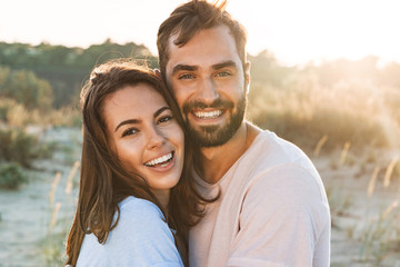 Beautiful young smiling couple spending time at the beach - obrazy, fototapety, plakaty