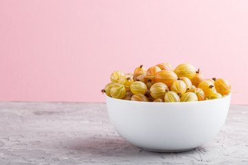 Fresh green gooseberry in white bowl on gray and pink background. side view.