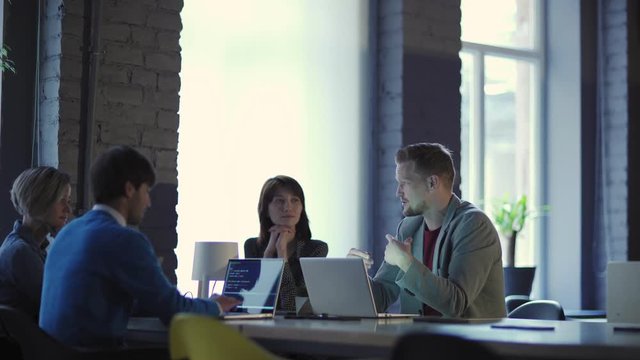 Group of four business people meeting at office and planning online project. Diverse group listening to middle aged team leader explaining his ideas, tracking shot