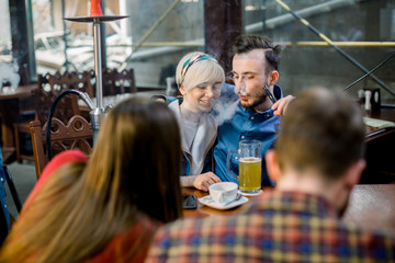 Group of friends having a meeting in cafe together. Focus on young couple, kissing and hugging at cafe talking laughing and enjoying their time.