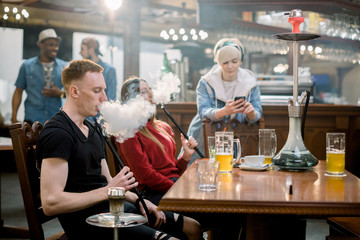 Group of young and beatiful people smoking hookah in the lounge cafe