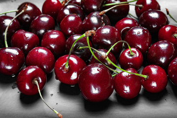 Ripe juicy wet cherries on a black plate. Wet fresh sweet cherries with water drops.
