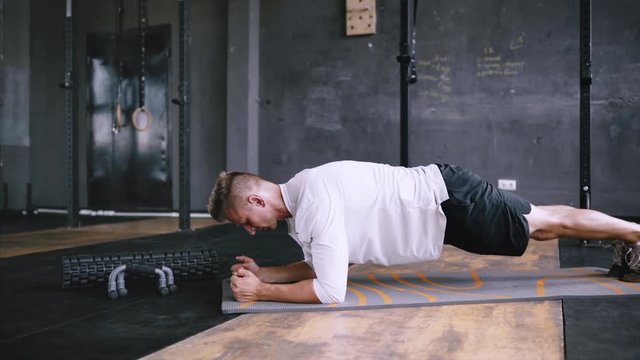 Athletic strong man does plank saws as part of his cross fitness, bodybuilding gym training routine. Intermediate no equipment exersize to endurance for abs and core. healthy man working out