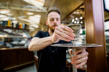 handsome young smiling barmen is preparing a device for smoking, hookah. close up photo.