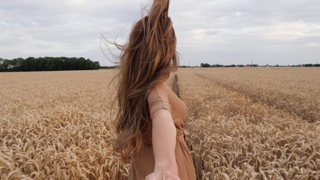 Happy young beautiful woman running in wheat field together holding hand with man pov camera folowing his wife