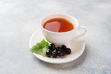 Cup of tea and fresh blackcurrant berries on grey table. Copy space.