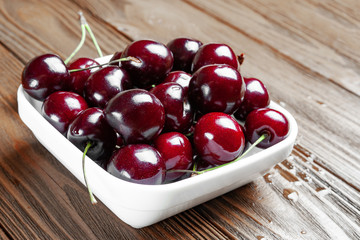 Red fresh ripe juicy sweet cherries in a white plate on a wooden background. Wet sweet cherries with water drops.