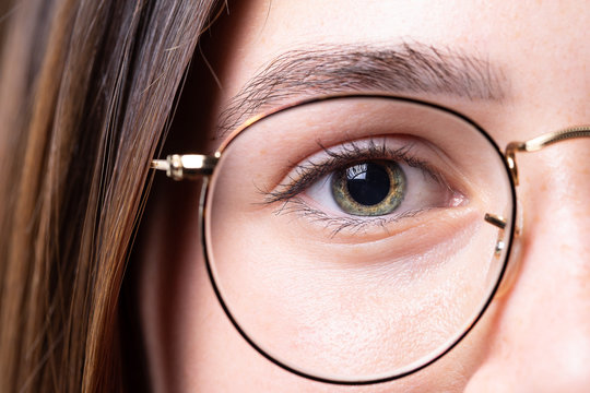 An attractive young Caucasian lady stares into the lens wearing reading glasses with gold rims. Brunette girl with copy space on the left.
