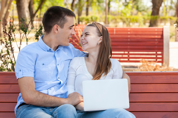 Couple using a laptop outdoors and looking happy.