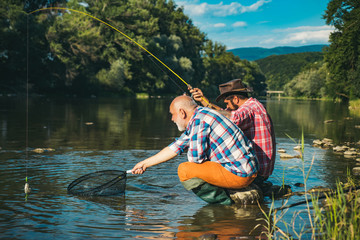 Fishermen with fishing rod on the river. Happy family concept - father and son together. Fisherman fishing with spinning reel.
