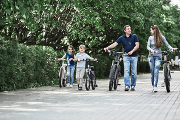 modern family with their bikes walk through the city Park
