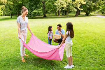 family, leisure and people concept - happy mother with daughter laying down picnic blanket on grass...