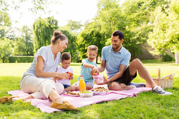 family, leisure and people concept - happy mother, father and two little sons having picnic at summer park - Powered by Adobe