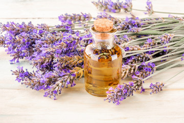 Obraz na płótnie Canvas Lavender essential oil in a glass bottle with a bouquet of fresh blooming lavender flowers on a rustic wooden background with copy space, toned image
