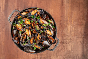 A full braiser of marinara mussels, shot from the top on a dark rustic background with a place for text