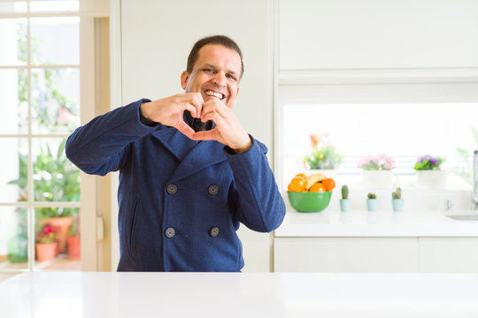 Middle age man sitting at home smiling in love showing heart symbol and shape with hands. Romantic concept.