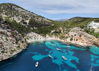 Naklejka premium Drone point of view aerial photo moored yachts on the bright blue bay on the Cala Blanca Andratx in the Palma de Mallorca, rocky coast breathtaking view, Balearic Islands Spain.