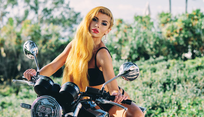 Fototapeta na wymiar Beautiful european woman with blond long hair wearing black lingerie sitting on motorcycle posing on nature