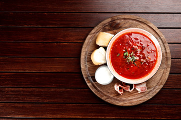 borsch with bacon and pampushkas on a wooden board on a brown wooden background