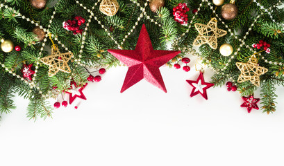Festive Christmas border, isolated on white background. Fir green branches are decorated big red star, gold stars, beads, fir cones and red berries. Close-up, copy space.