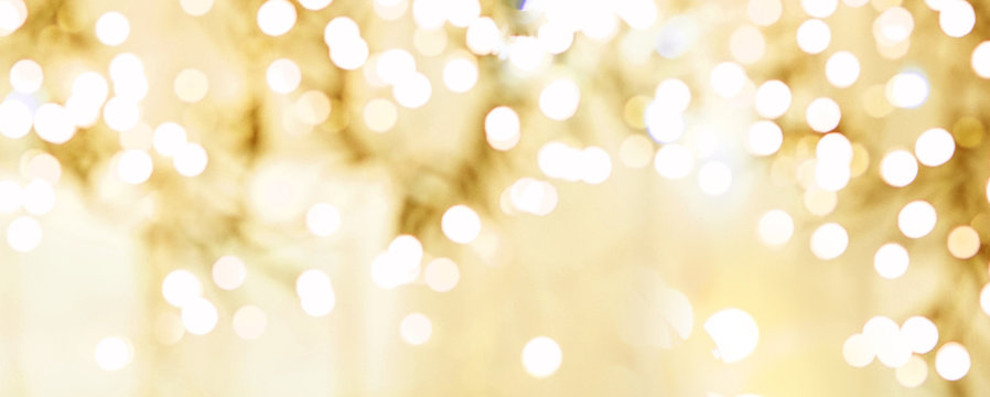 Festive abstract defocused Christmas background. Golden Christmas lights sparkle, beautiful round bokeh, wide banner format, copy space.