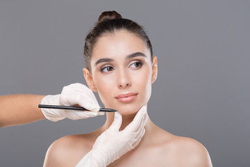 Doctor drawing lines on female face, gray studio background