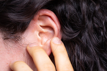 A young Caucasian girl, hard of hearing, is seen close up pointing towards her ear with her...