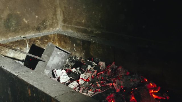 The red and dark gray coals inside the brazier are mixed with a metal scoop. Preparation for cooking kebabs in 4k resolution