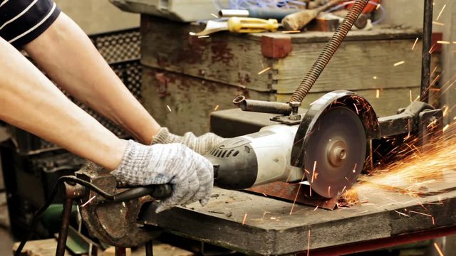 Cinemagraph: A man cuts a metal corner with a cutting wheel on a homemade machine in a home workshop. Worker using industrial grinder works circular saw. Flies of spark from hot metal. Man's hard work