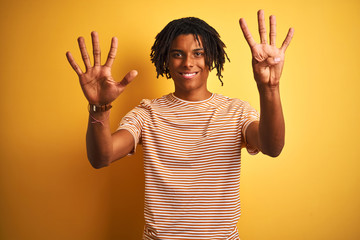 Afro man with dreadlocks wearing striped t-shirt standing over isolated yellow background showing...