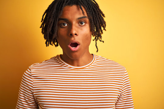 Afro man with dreadlocks wearing striped t-shirt standing over isolated yellow background scared in shock with a surprise face, afraid and excited with fear expression