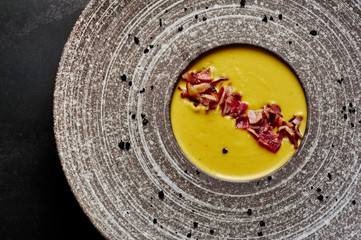 Pumpkin squash cream soup with bacon in big plate at black background. Pumpkin soup is traditional...