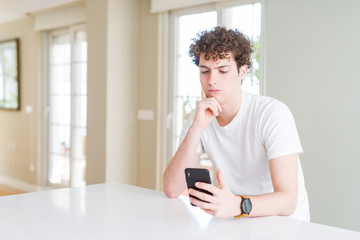 Young man using smartphone at home serious face thinking about question, very confused idea