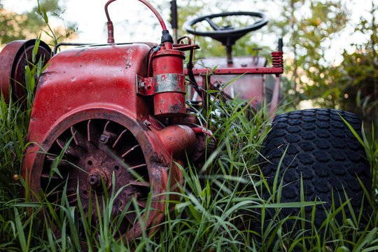 Close up of abandoned red tractor wreck, overgrown with long green grass on a farm.