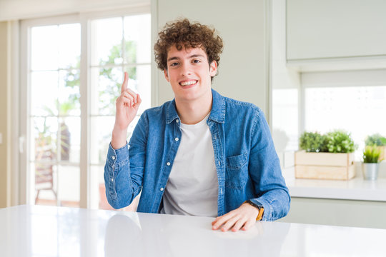Young handsome man wearing casual denim jacket at home pointing finger up with successful idea. Exited and happy. Number one.
