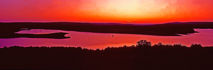 An impressive sunset over Kielder Water Northumberland with single yacht sailing away from the Marina