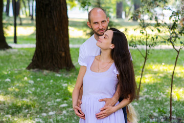 Fototapeta premium Portrait of happy loving couple hugging tenderly and warmly in the park and expecting the arrival of newborn.
