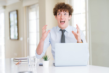 Young business man working with computer laptop at the office crazy and mad shouting and yelling with aggressive expression and arms raised. Frustration concept.