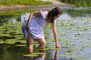 Young pregnant woman in the water touching the beautiful water lilies in the river