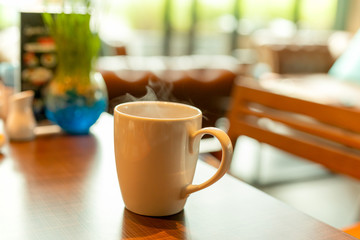 White ceramics coffee mug with smoke and small plant on wooden table in cafe.