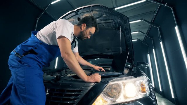 Male mechanic is fixing a car with the help of a computer