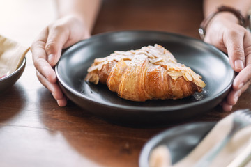 A woman holding and showing a dish of fresh almond croissant