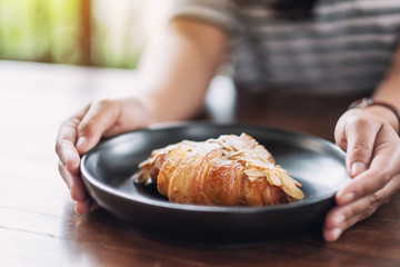 A woman holding and showing a dish of fresh almond croissant